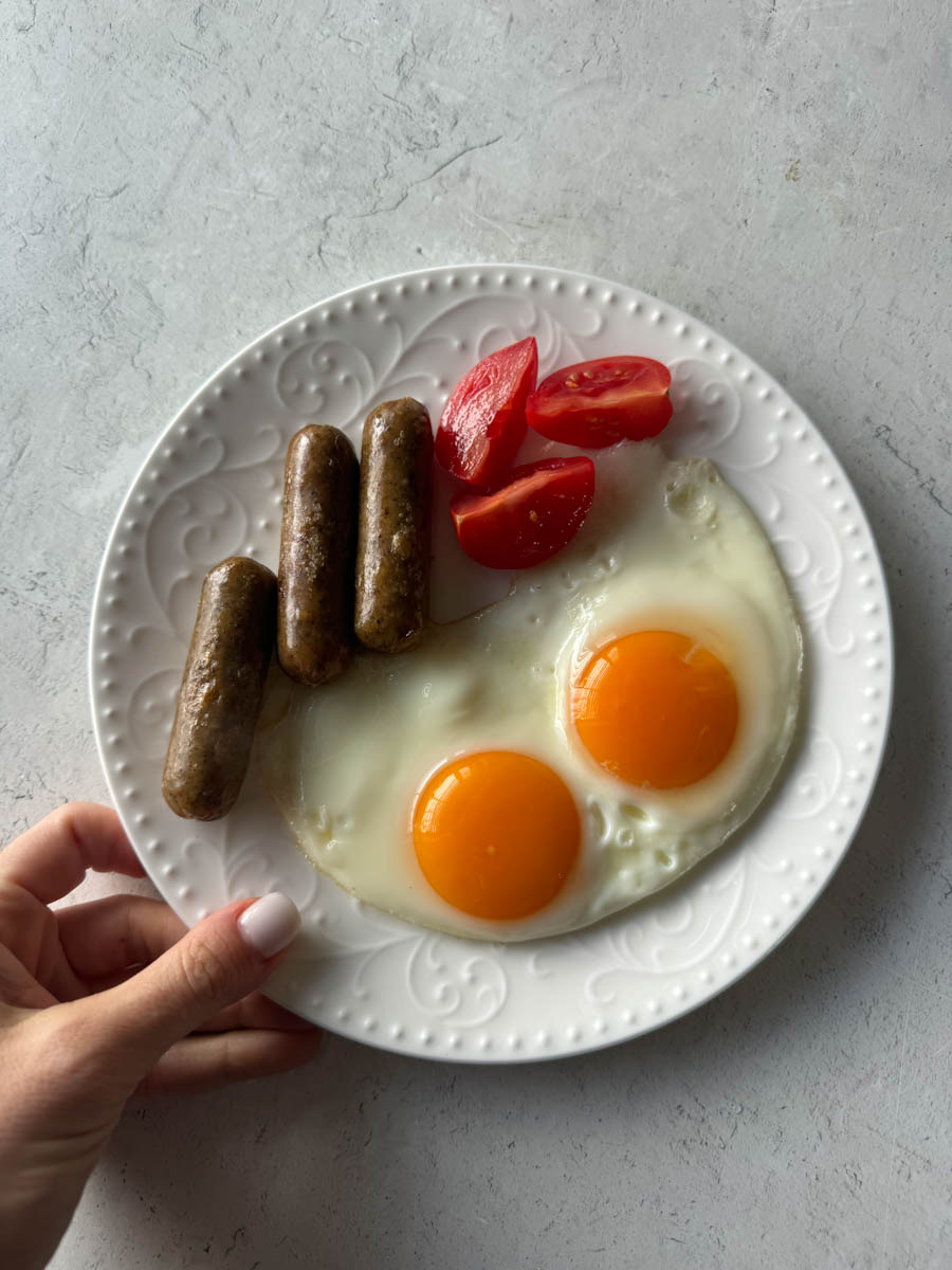 two cooked eggs, chicken breakfast links and tomatoes on the plate