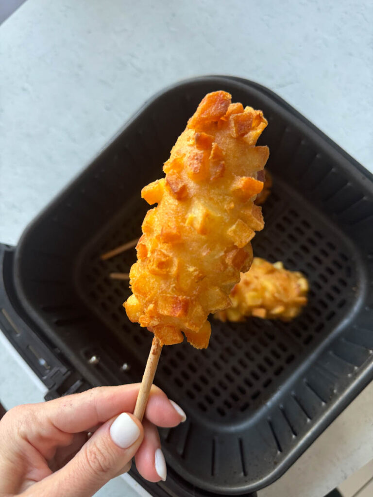 holding a costco crispy potato corn dog above the air fryer basket