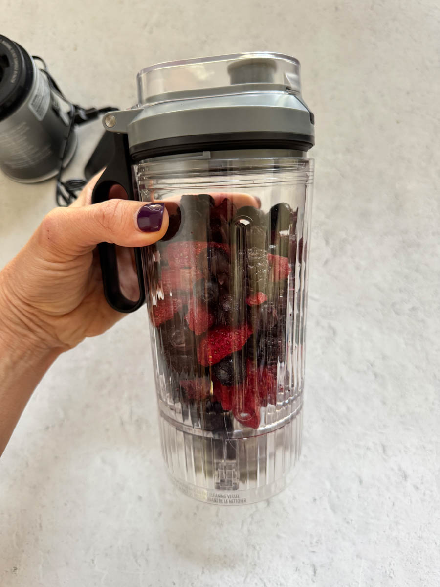 holding a blender in hand with berries in it