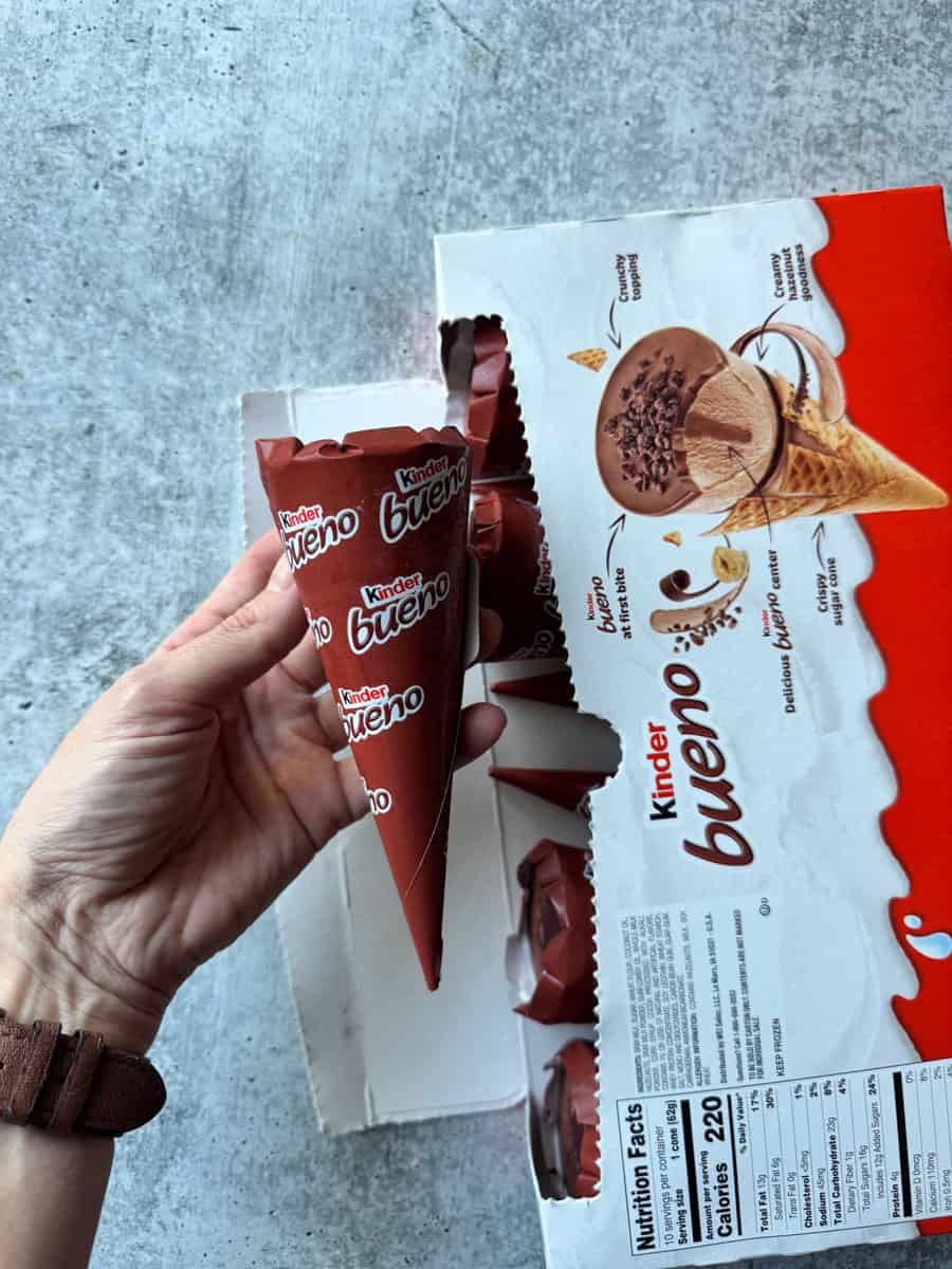 Hand holding Kinder Bueno ice cream cone with packaging on a gray surface.