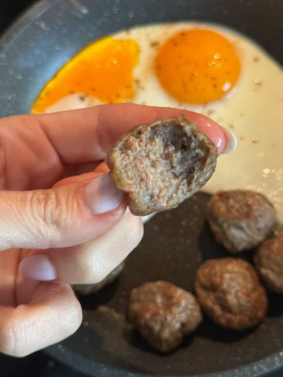 Close-up of homemade meatballs cooking in a skillet with fried eggs in the background.
