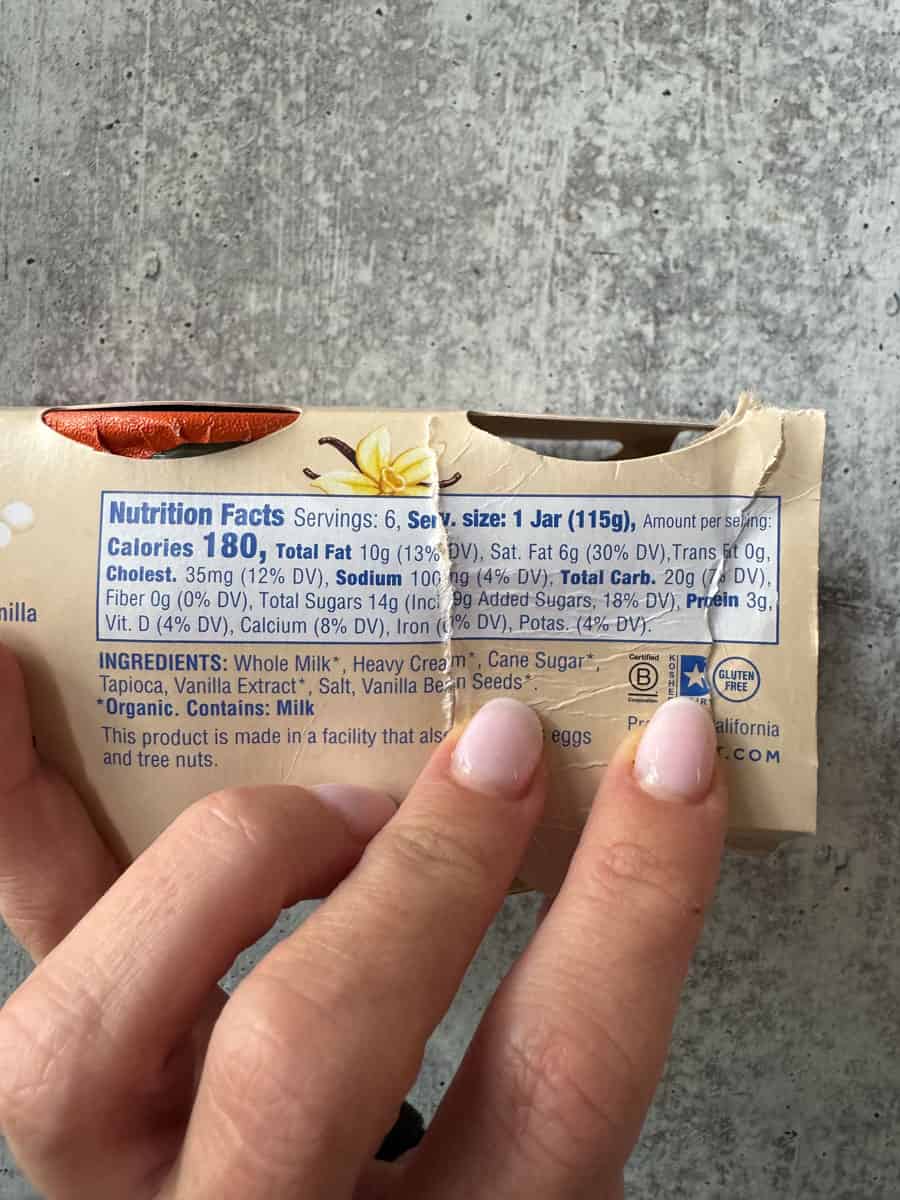 Organic vanilla extract in a small bottle, held by fingers on a gray surface.