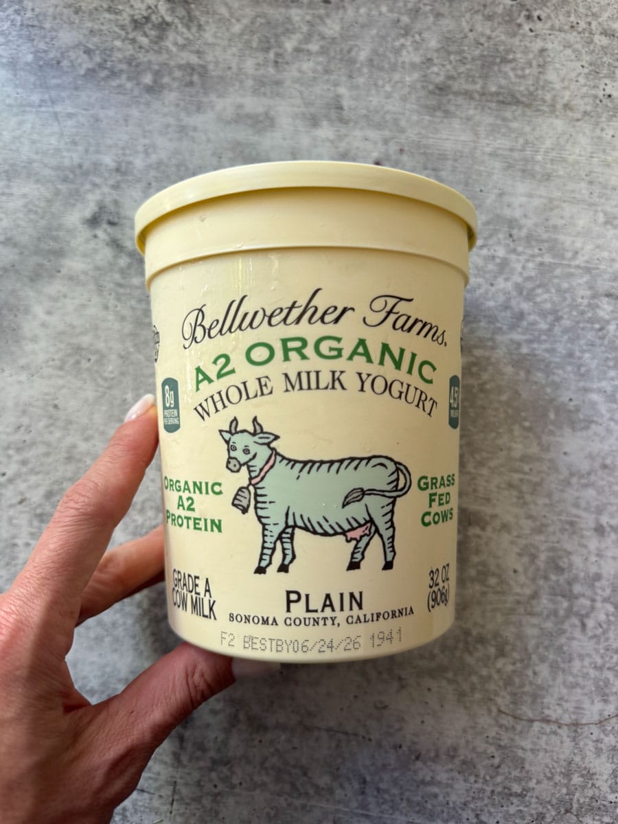 Bellwether Farms organic plain A2 milk yogurt in a beige container held by hand.