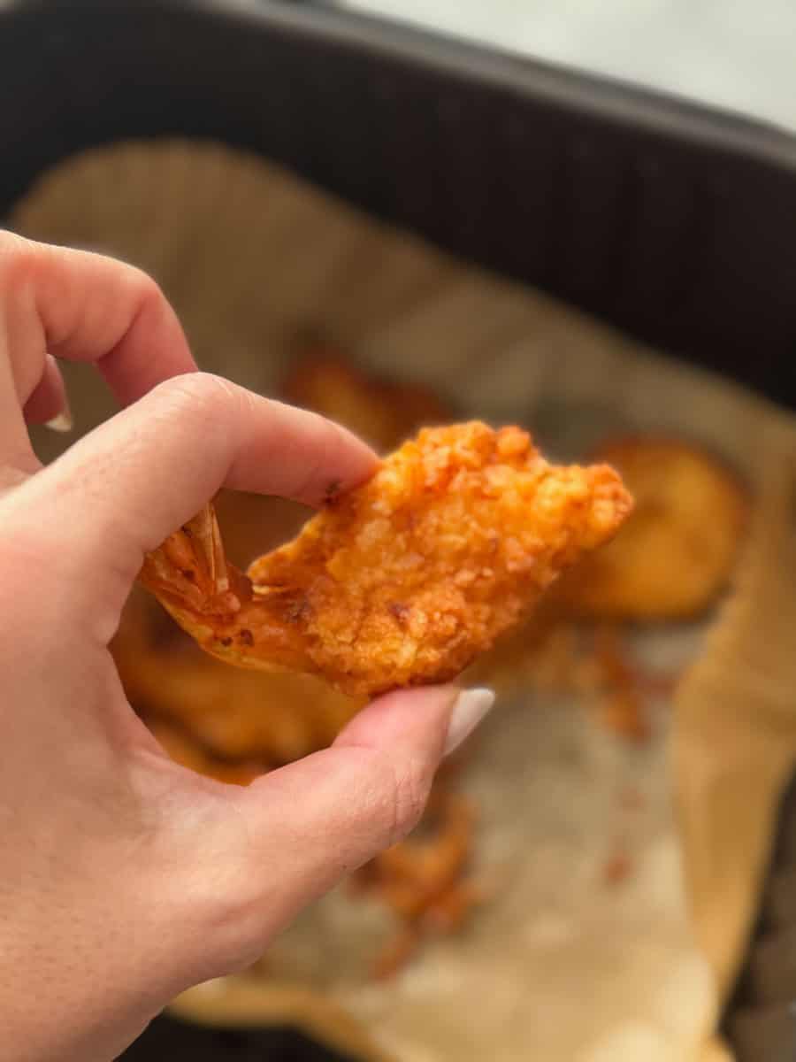 Hand holding a crispy fried chicken tender over a basket of chicken tenders.