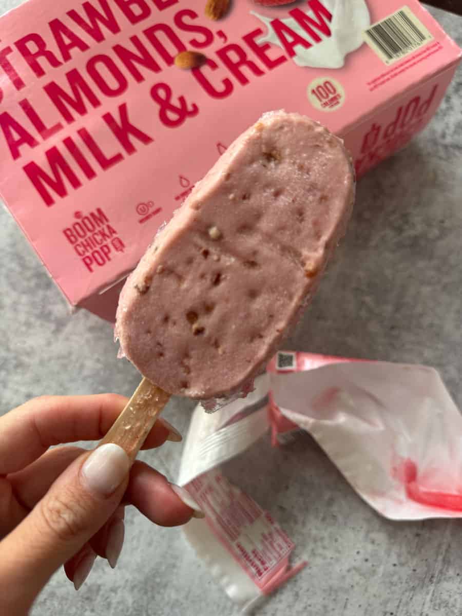Strawberry almond milk ice cream bar with nuts, in pink packaging, on a gray surface.
