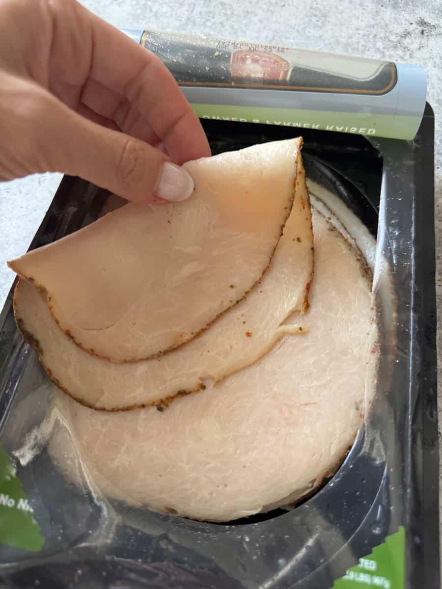 Close-up of hand peeling sliced turkey breast from Costco package, ready for meal prep.