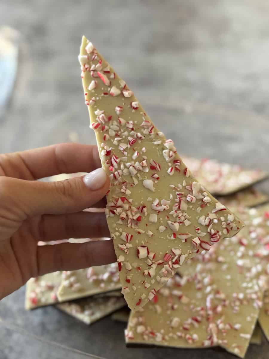 Hand holding white chocolate peppermint bark with crushed peppermint pieces.