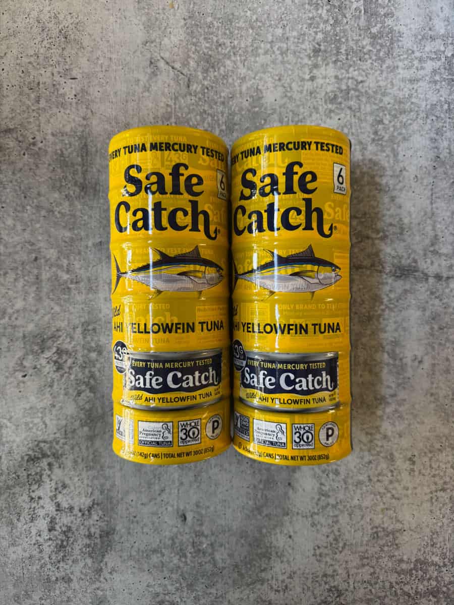 Two yellow Safe Catch tuna cans on a concrete surface.