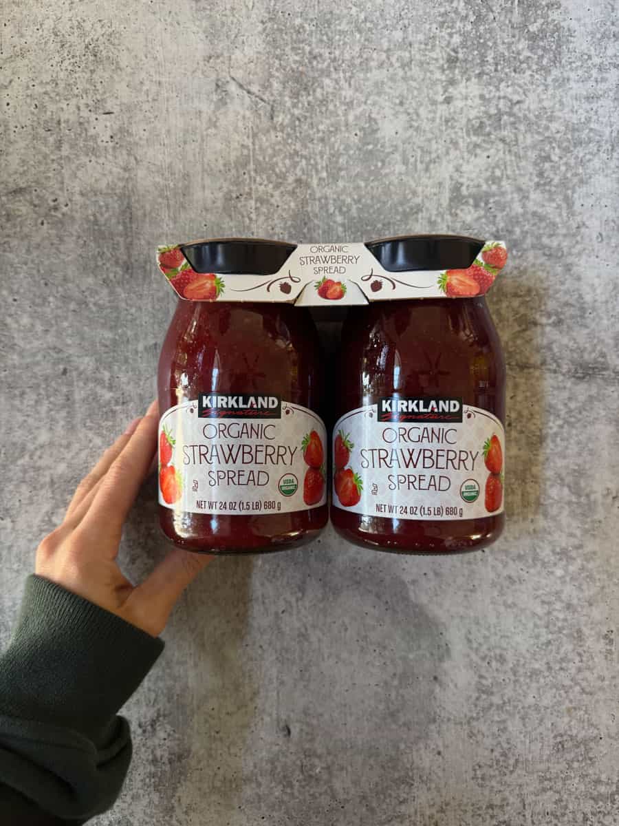 Organic strawberry spread jars by Kirkland with hand holding.