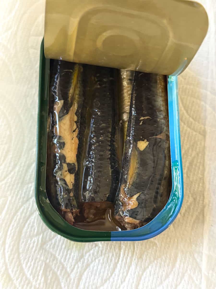Canned fish in open can with foil lid showing shiny contents.